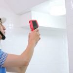 close up asian male home inspector is using thermal imager to check water leakage situation on wall